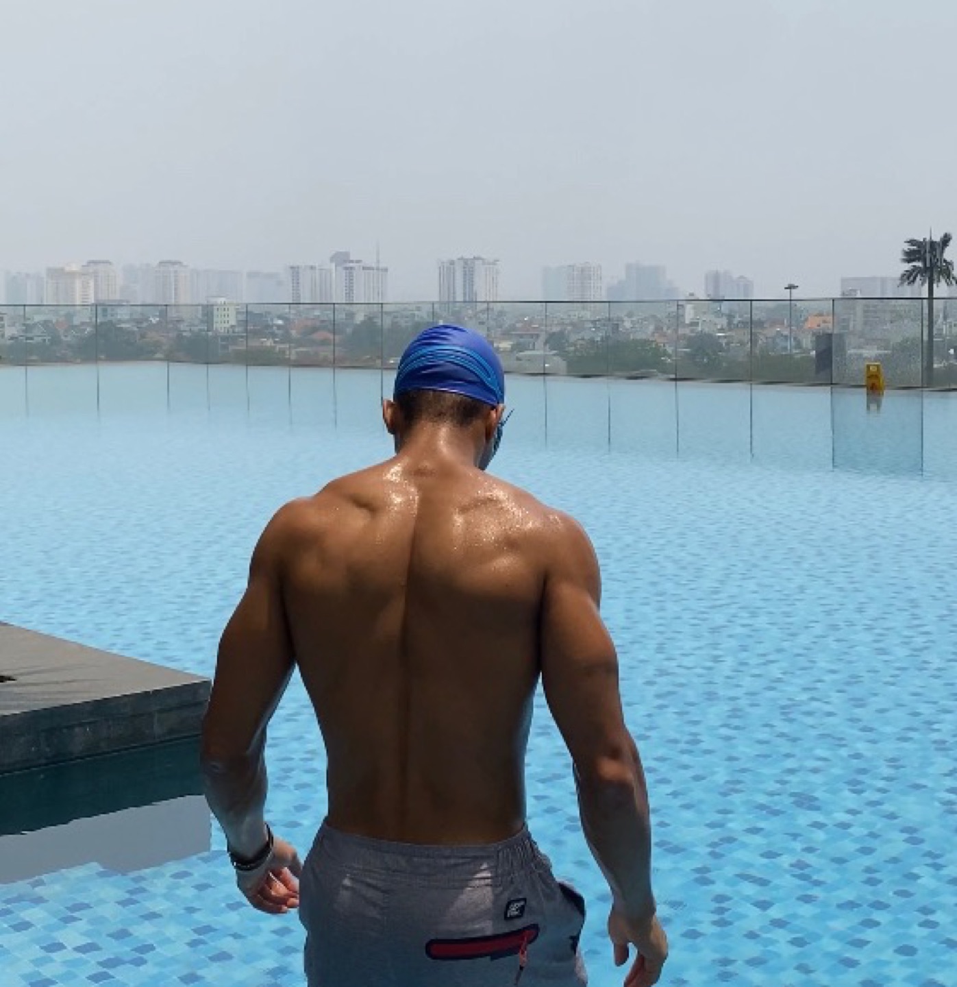 OYOTTA in blue head covering beside a rooftop pool, seen from behind